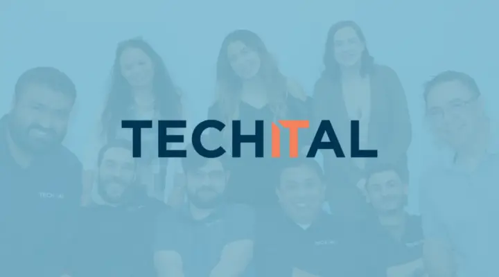 Techital team standing in front of white wall for group photo with blue overlay and Techital logo