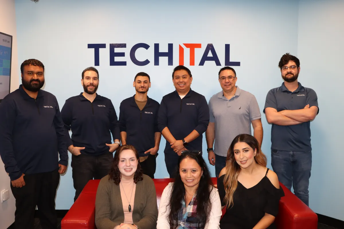 Techital Team standing - sitting on sofa in front of logo on wall